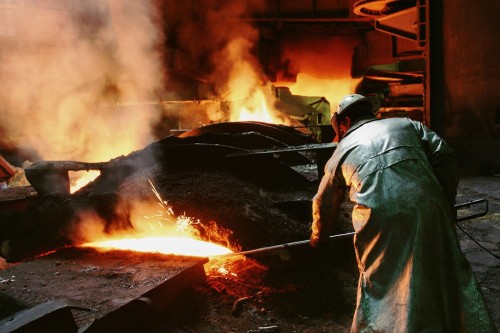 Photo argentique de reportage dans une usine sidérurgique. Homme au travail vêtu d' une combinaison ignifugé et d'un casque de protection devant une coulé de métal en fusion. | Philippe DUREUIL Photographie